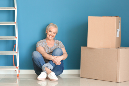 Mature woman with moving boxes sitting on floor at new homeの写真素材