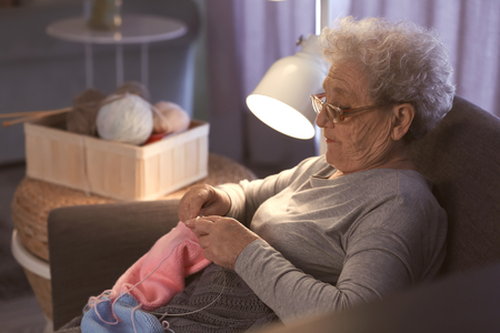 Senior woman knitting warm sweater in armchair at homeの写真素材