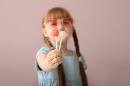Cute little girl with lollipops on color backgroundの写真素材