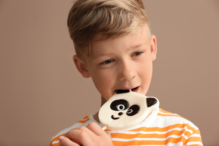 Cute little boy eating lollipop on color backgroundの写真素材