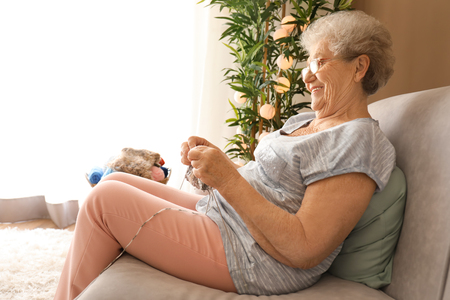 Senior woman knitting warm scarf at homeの写真素材