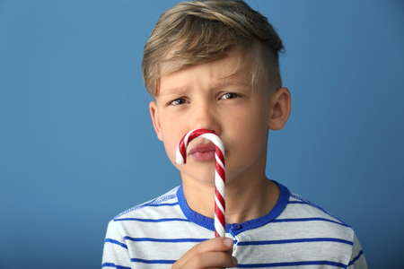 Cute little boy with candy cane on color backgroundの写真素材