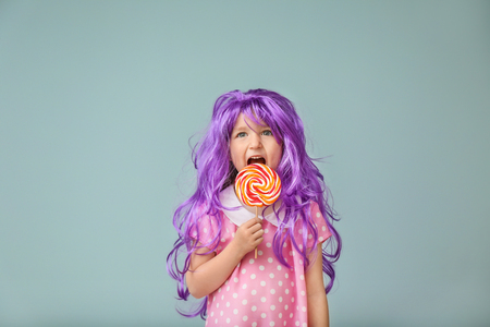 Cute little girl in purple wig and with lollipop on color backgroundの写真素材