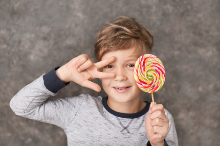 Cute little boy with lollipop on grey background