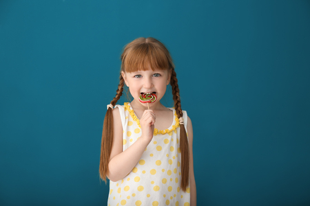 Cute little girl eating lollipop on color backgroundの写真素材