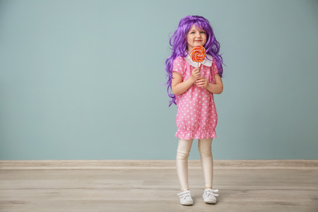 Cute little girl in purple wig and with lollipop near color wallの写真素材