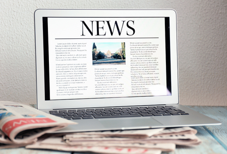 Laptop with open news page and newspapers on tableの写真素材