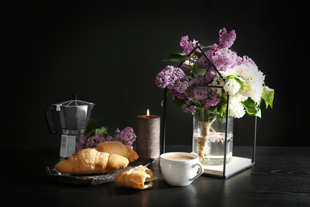 Tasty croissants with cup of coffee and beautiful blossoming lilac on tableの写真素材