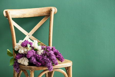 Beautiful blossoming lilac on chair against color backgroundの写真素材