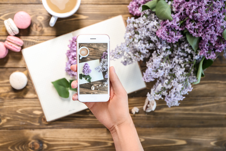 Woman taking photo of blossoming lilac and cup with coffeeの写真素材