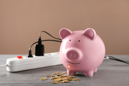 Piggy bank, coins and power strip on table. Electricity saving conceptの写真素材