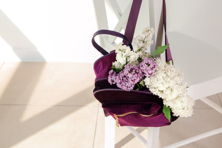 Backpack with beautiful blossoming lilac on chair indoorsの写真素材