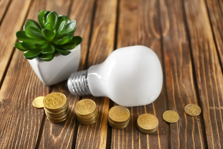 Light bulb and stacked coins on wooden background. Electricity saving conceptの写真素材