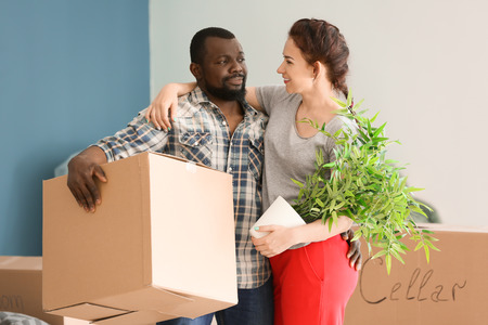 Interracial couple with plant and boxes indoors. Moving into new house