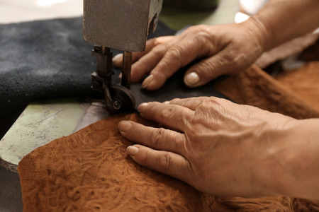 Mature woman using sewing machine in leather workshop, closeupの写真素材