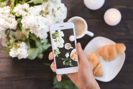 Woman taking photo of blossoming lilac and croissant with coffeeの写真素材
