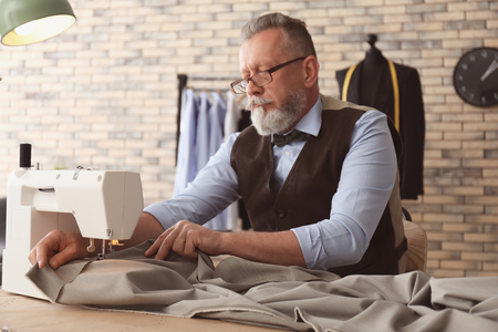 Mature tailor working on sewing machine in atelierの写真素材