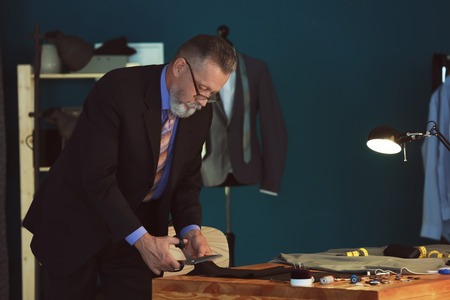 Mature tailor cutting fabric in atelierの写真素材