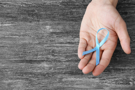 Male hand with blue ribbon on wooden background. Prostate cancer conceptの写真素材
