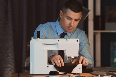 Young tailor working on sewing machine in atelier