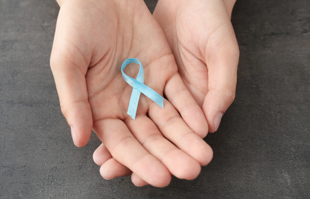 Male hands holding blue ribbon on grey background. Prostate cancer concept