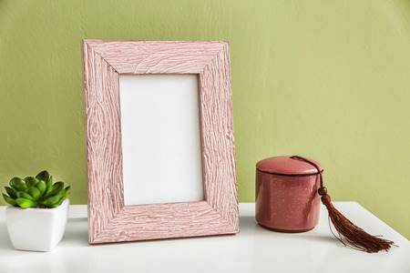 Photo frame with plant and candle in holder on white table against color backgroundの写真素材