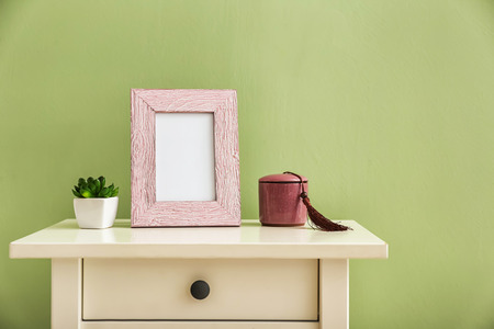 Photo frame with plant and candle in holder on white table against color background