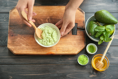 Young woman making nourishing mask with avocado at tableの写真素材