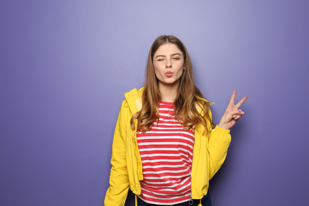 Beautiful young woman showing Victory gesture on color backgroundの写真素材