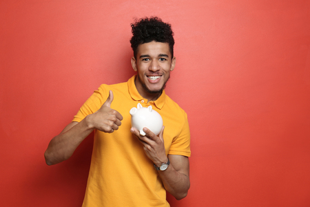 African-American man with piggy bank on color backgroundの写真素材