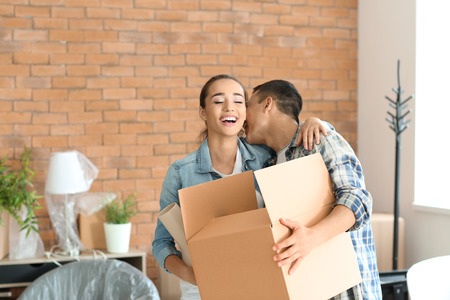 Young couple with box and vase indoors. Moving into new house