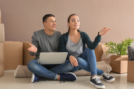 Young couple with laptop sitting on floor near boxes indoors. Moving into new houseの写真素材
