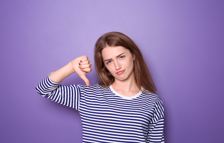 Beautiful young woman showing thumb-down gesture on color backgroundの写真素材