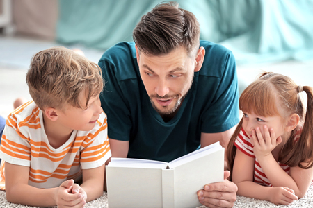 Father and his children reading book together at homeの写真素材