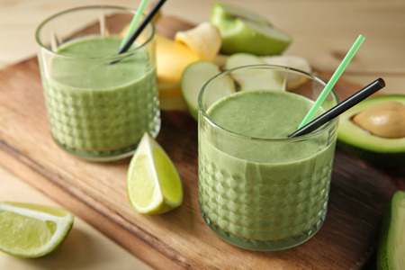 Glasses of tasty avocado smoothie and ingredients on wooden boardの写真素材