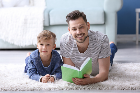 Father and his son reading book together at homeの写真素材