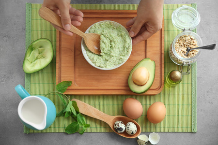 Young woman making nourishing mask with avocado at tableの写真素材
