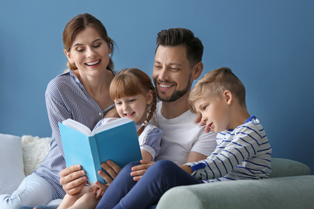 Parents and their children reading book together at homeの写真素材