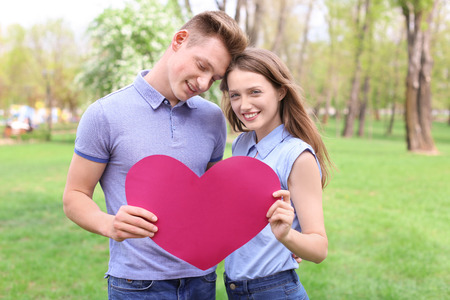 Happy young couple with paper heart in park on spring dayの写真素材