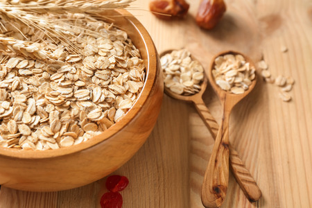 Bowl and spoons with oatmeal flakes on wooden tableの写真素材