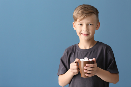Cute little boy with cup of hot cocoa drink on color backgroundの写真素材