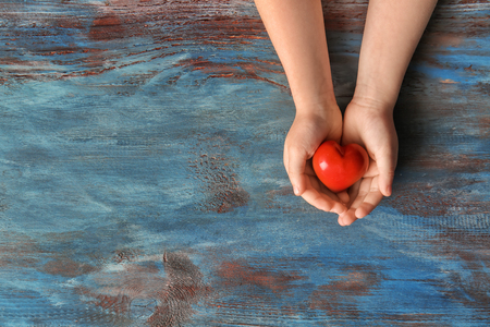 Hands of child with red heart on wooden backgroundの写真素材