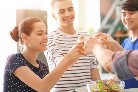 Young friends clinking glasses with juice in kitchenの写真素材