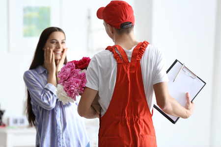 Young woman receiving beautiful flowers from delivery manの写真素材