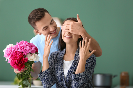 Young man giving beautiful flowers to his beloved girlfriend indoorsの写真素材