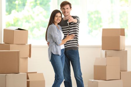 Young happy couple with key of their new house and moving boxes indoorsの写真素材