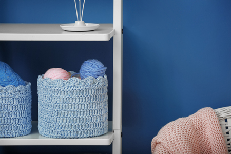 Baskets with balls of knitting yarn on shelf against color wallの写真素材