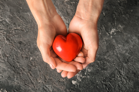 Hands of woman with red heart on dark textured backgroundの写真素材