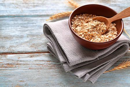 Bowl with raw oatmeal on wooden background