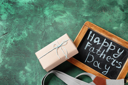 Happy Father's Day inscription on chalkboard with suspenders and gift box on color textured backgroundの写真素材